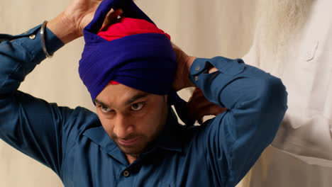 Close-Up-Studio-Shot-Of-Two-Sikh-Men-Tying-Fabric-For-Turban-Against-Plain-Background-3